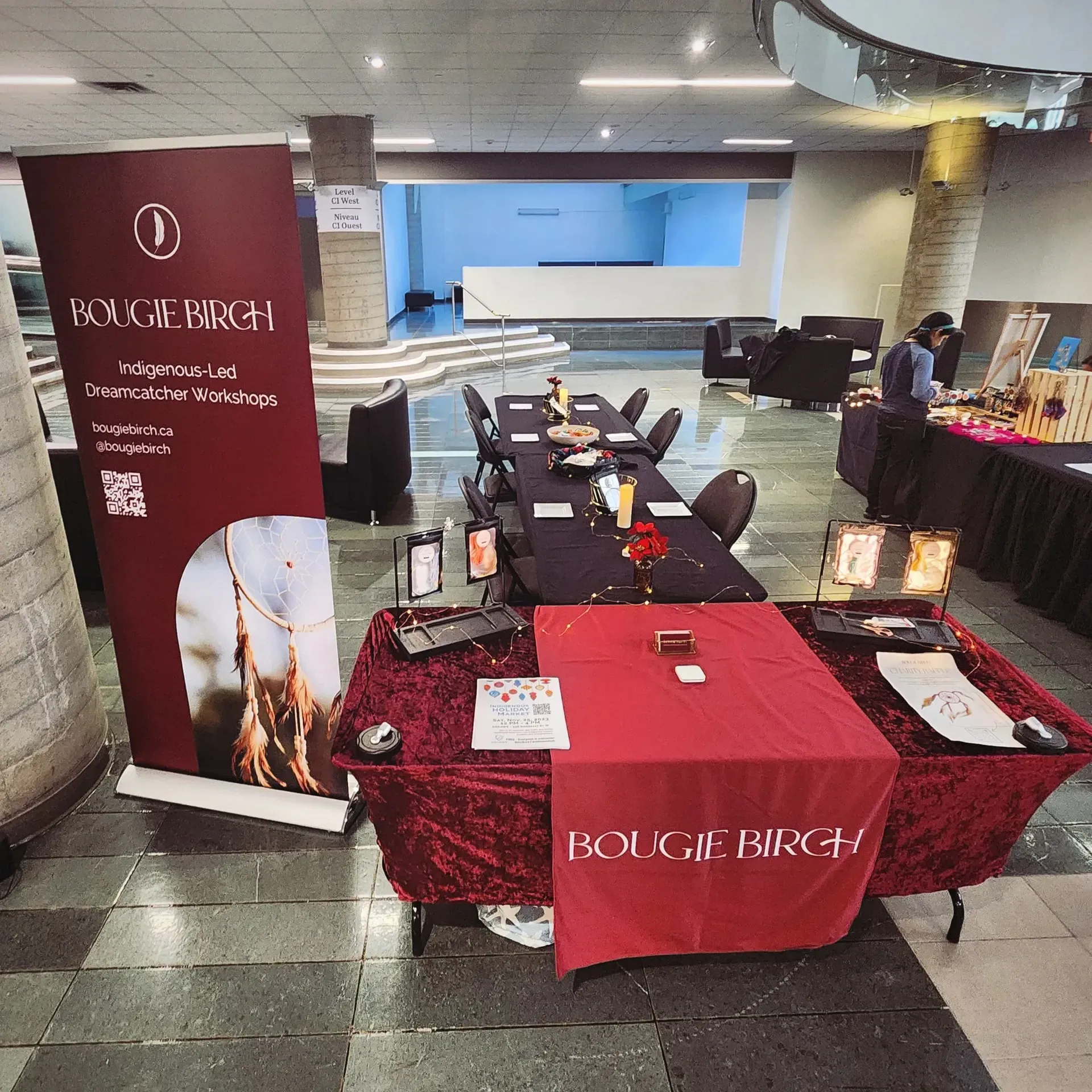 Event booth with a burgundy banner and tablecloth, candles, and jewelry. Inside a building.