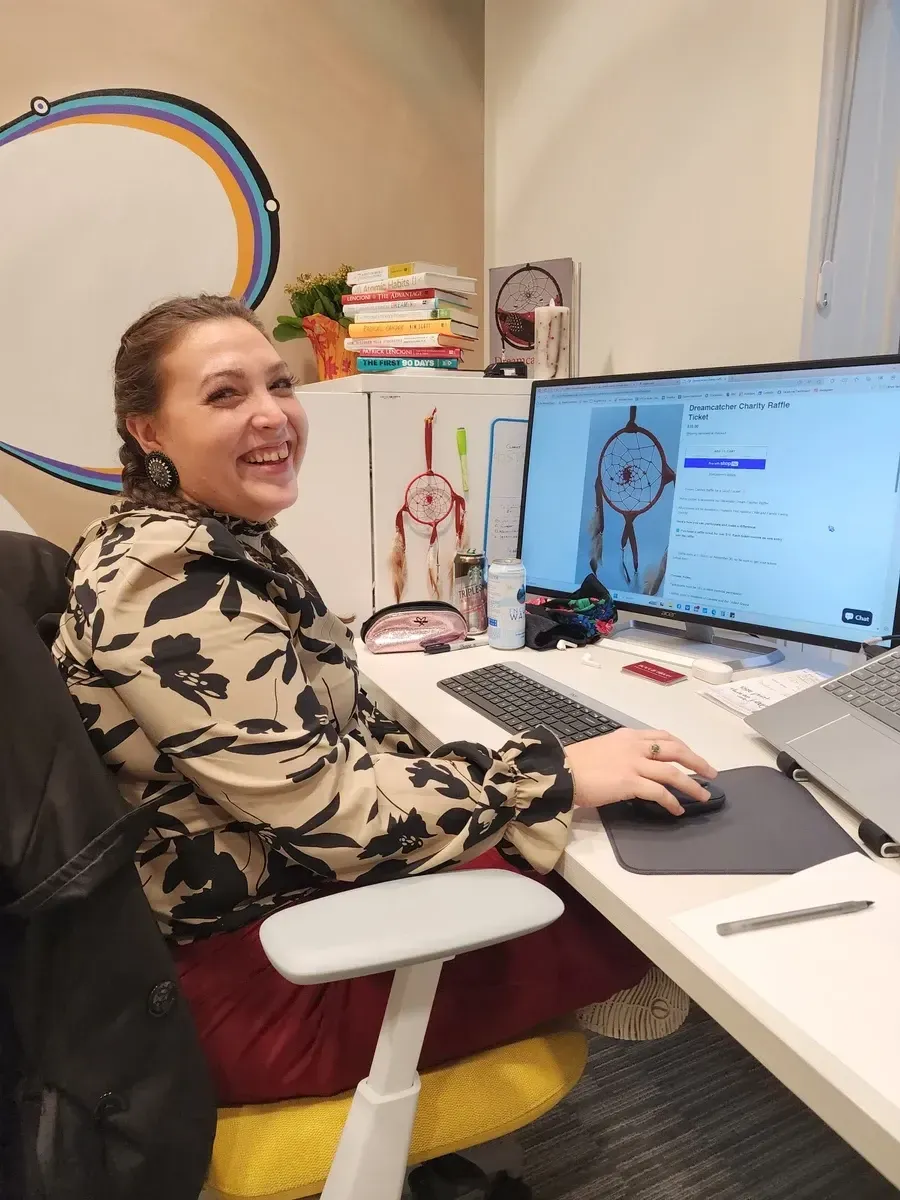Woman smiling at desk with computer, looking at dream catcher online.