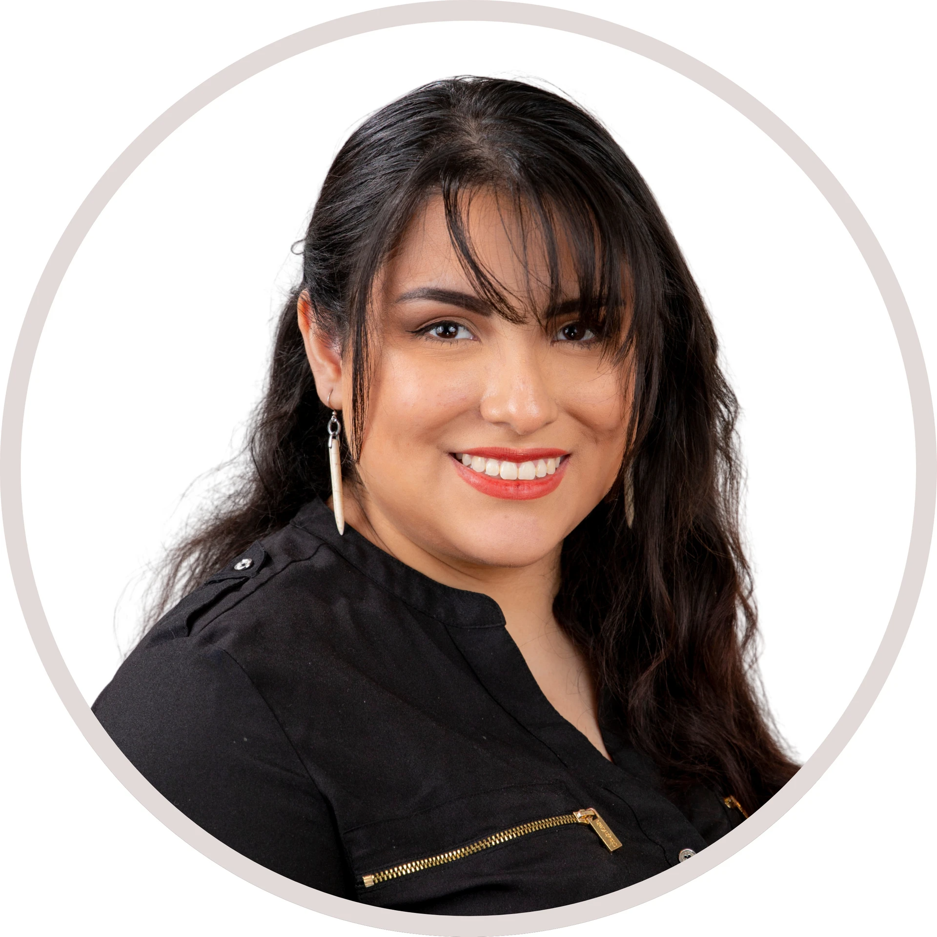 Woman with dark hair, bangs, smiling, wearing a black shirt with gold zippers and dangling earrings.