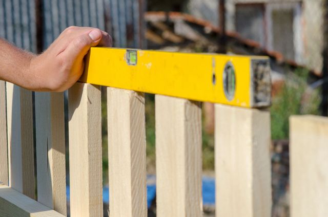 Man building a wooden fence and checking with a spirit level. Close-up of his hand and tool.