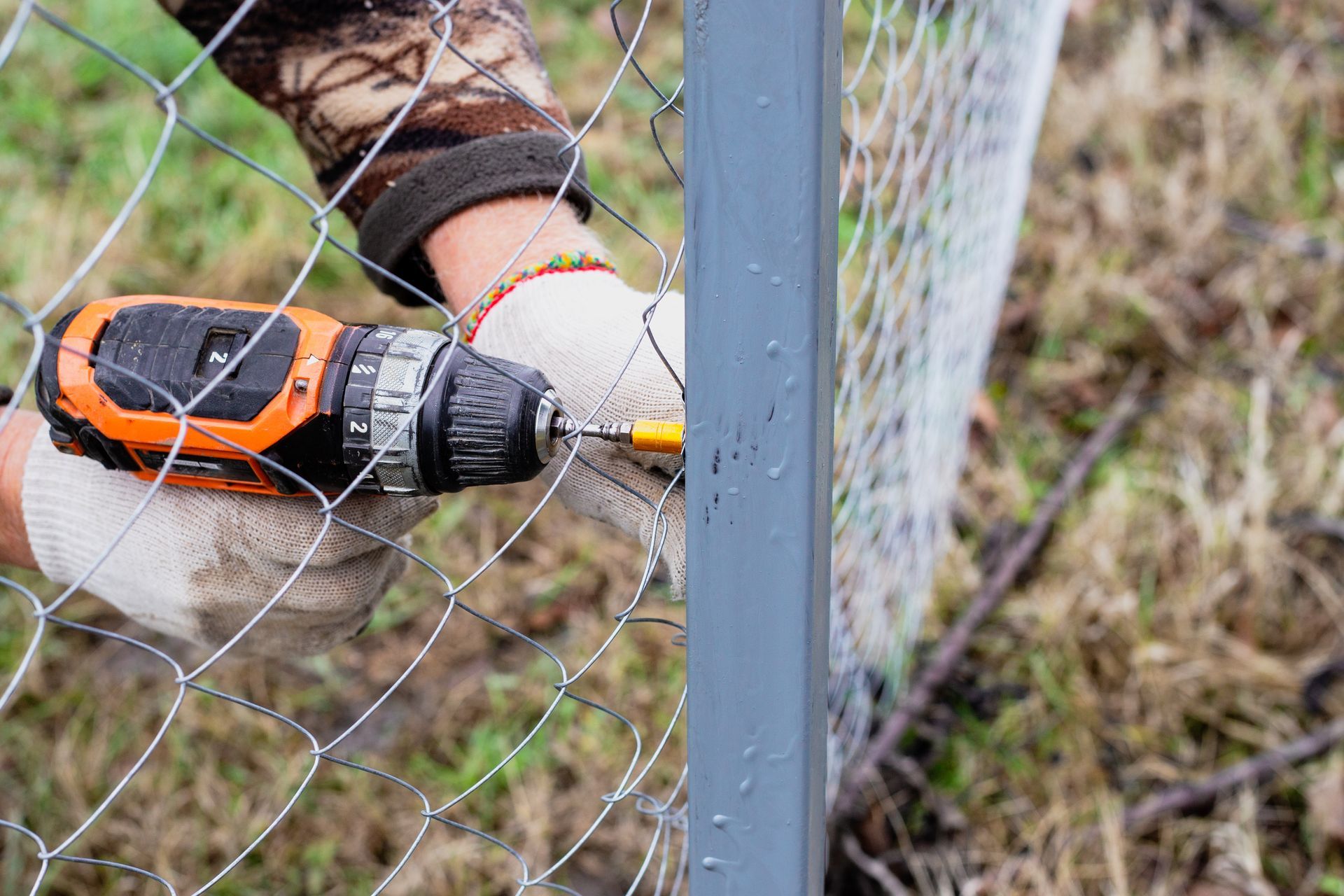 A worker using an electric drill screws a metal mesh chain-link to a metal profile. A worker using an electric drill screws a metal mesh chain-link to a metal profile.