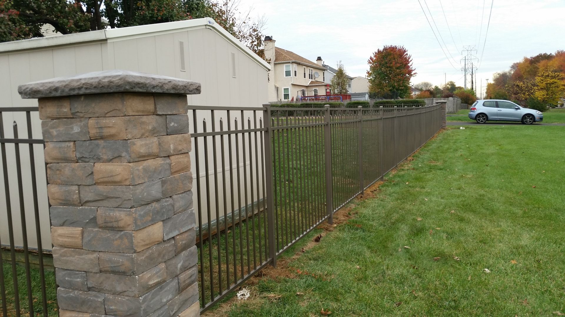A fence with a stone pillar and a car parked behind it.