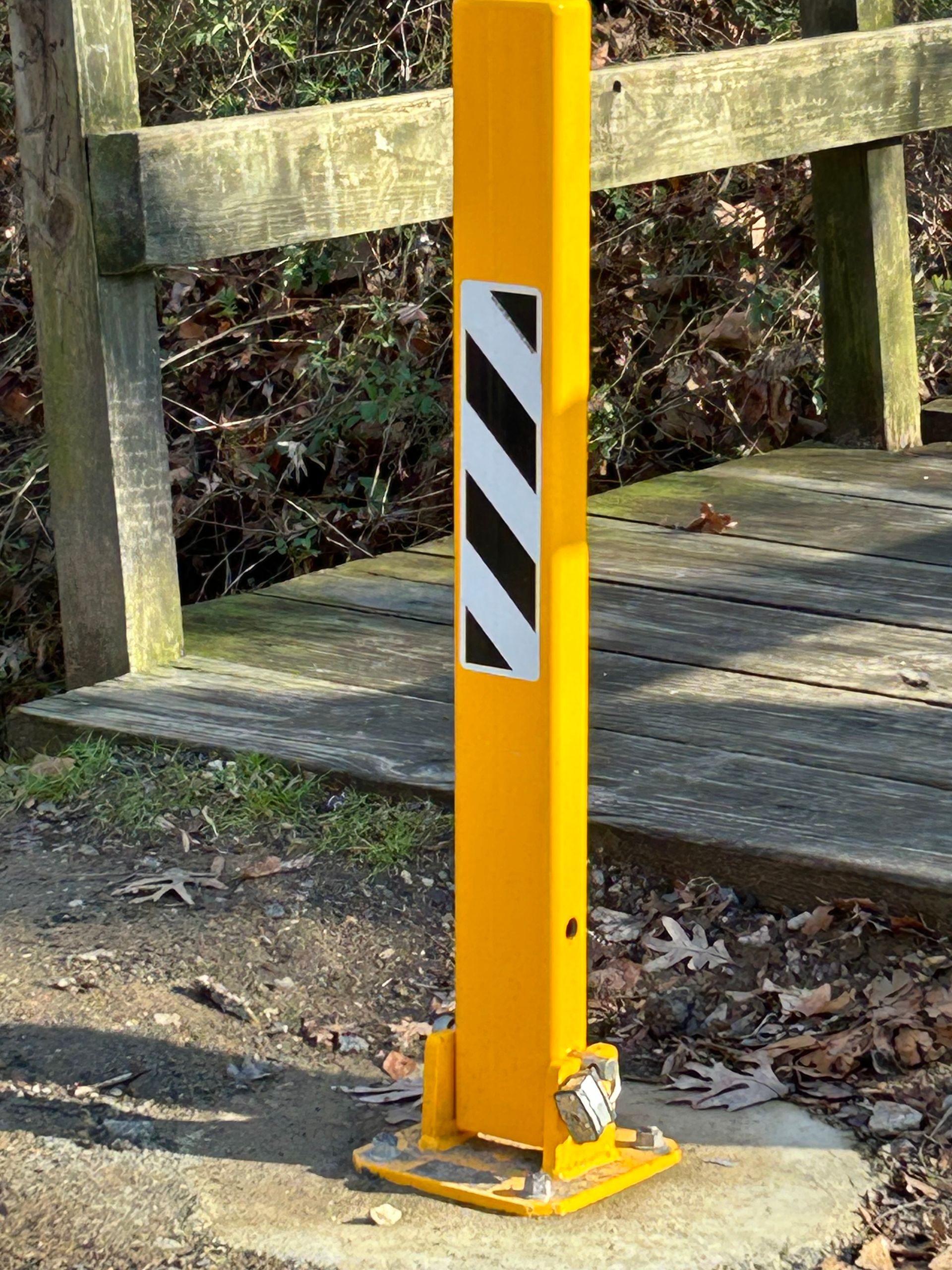 A yellow pole with black and white stripes on it is next to a wooden bridge.