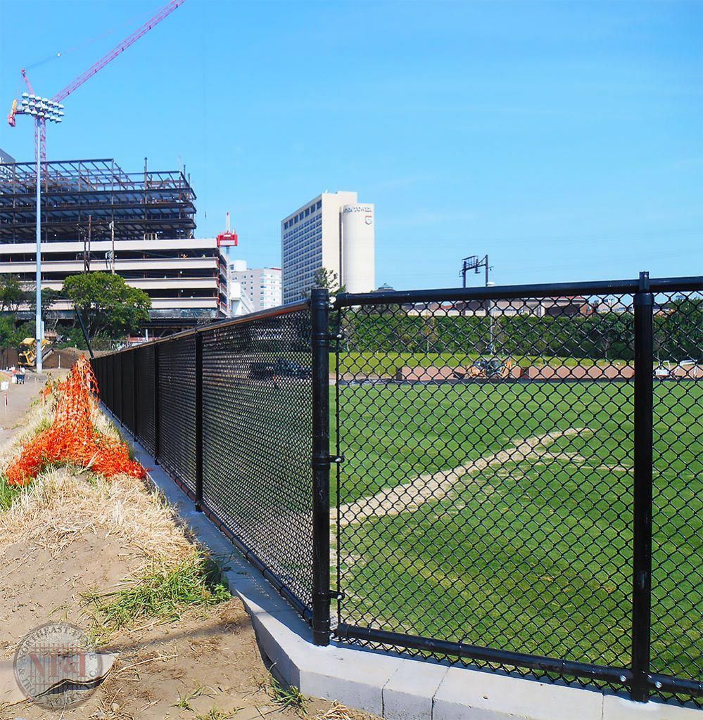 A chain link fence surrounds a field with a building in the background