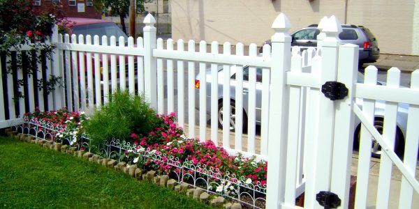 A white picket fence surrounds a garden with flowers.