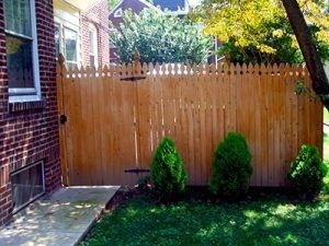 A wooden fence is in the backyard of a brick house.