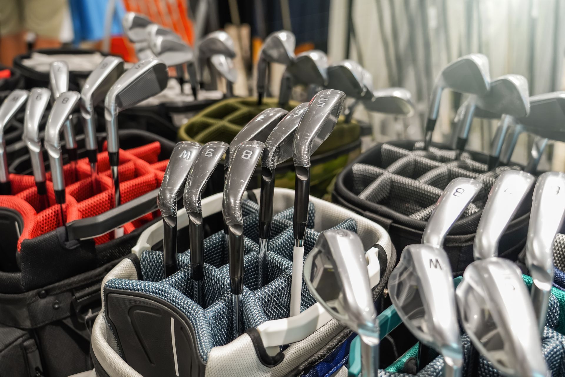 A bunch of golf clubs are sitting in golf bags.