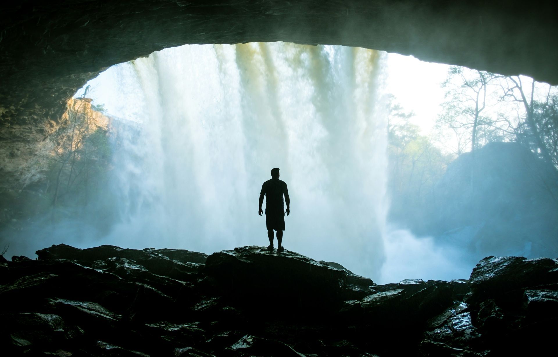 A man is standing in front of a waterfall in a cave.