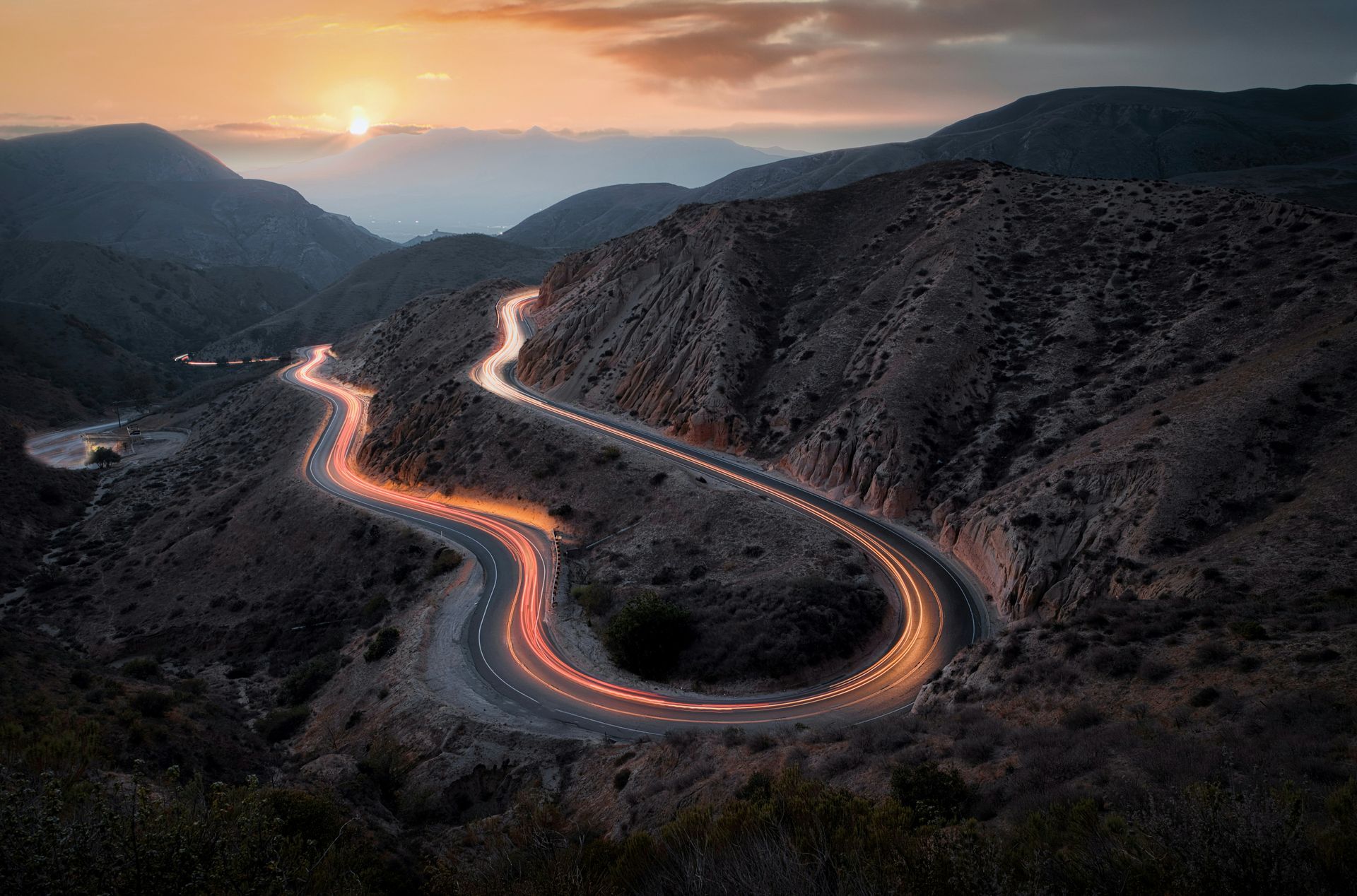 A long exposure photo of a winding road in the mountains at sunset.