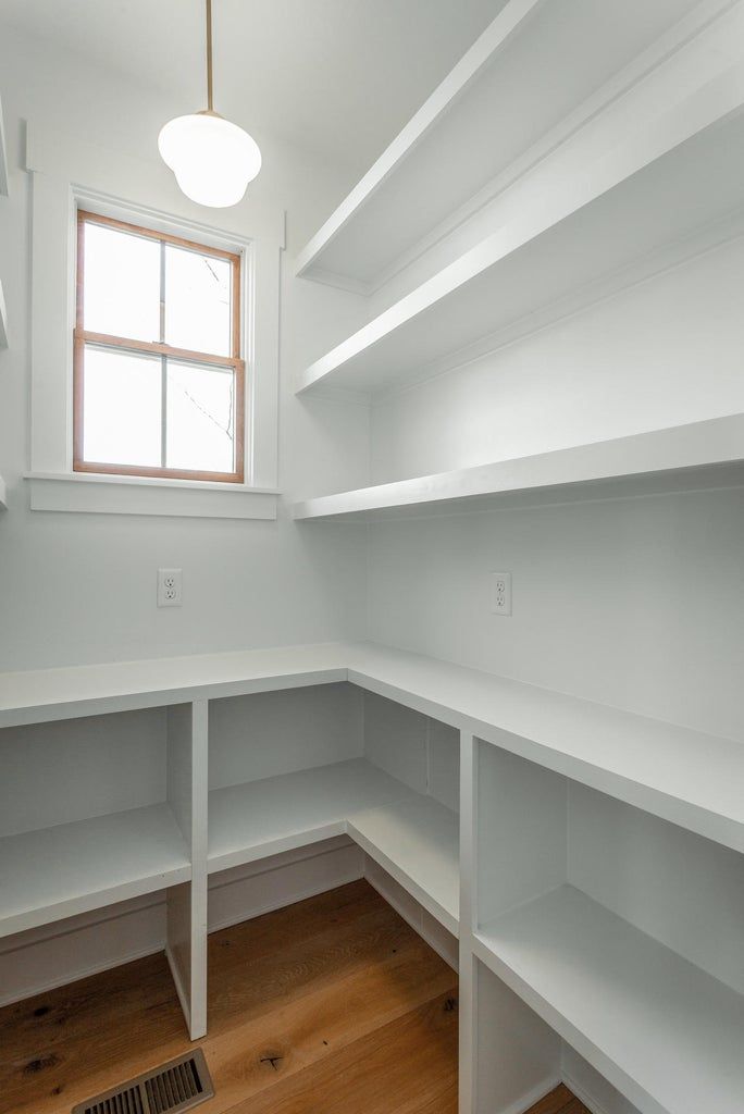 An empty pantry with white shelves and a window.
