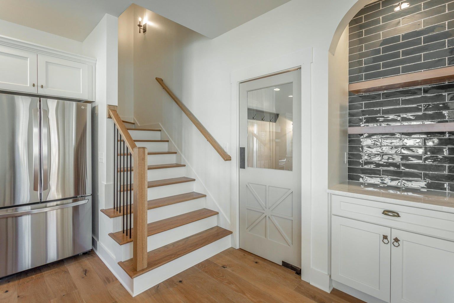 A kitchen with stairs leading up to the second floor and a refrigerator.