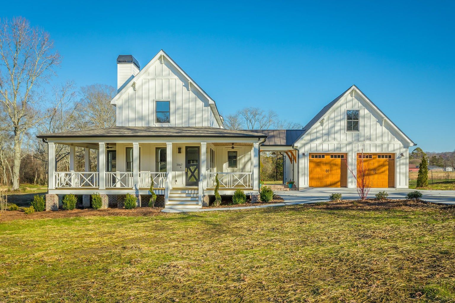 A large white house with a large porch and two garages is sitting on top of a lush green field.