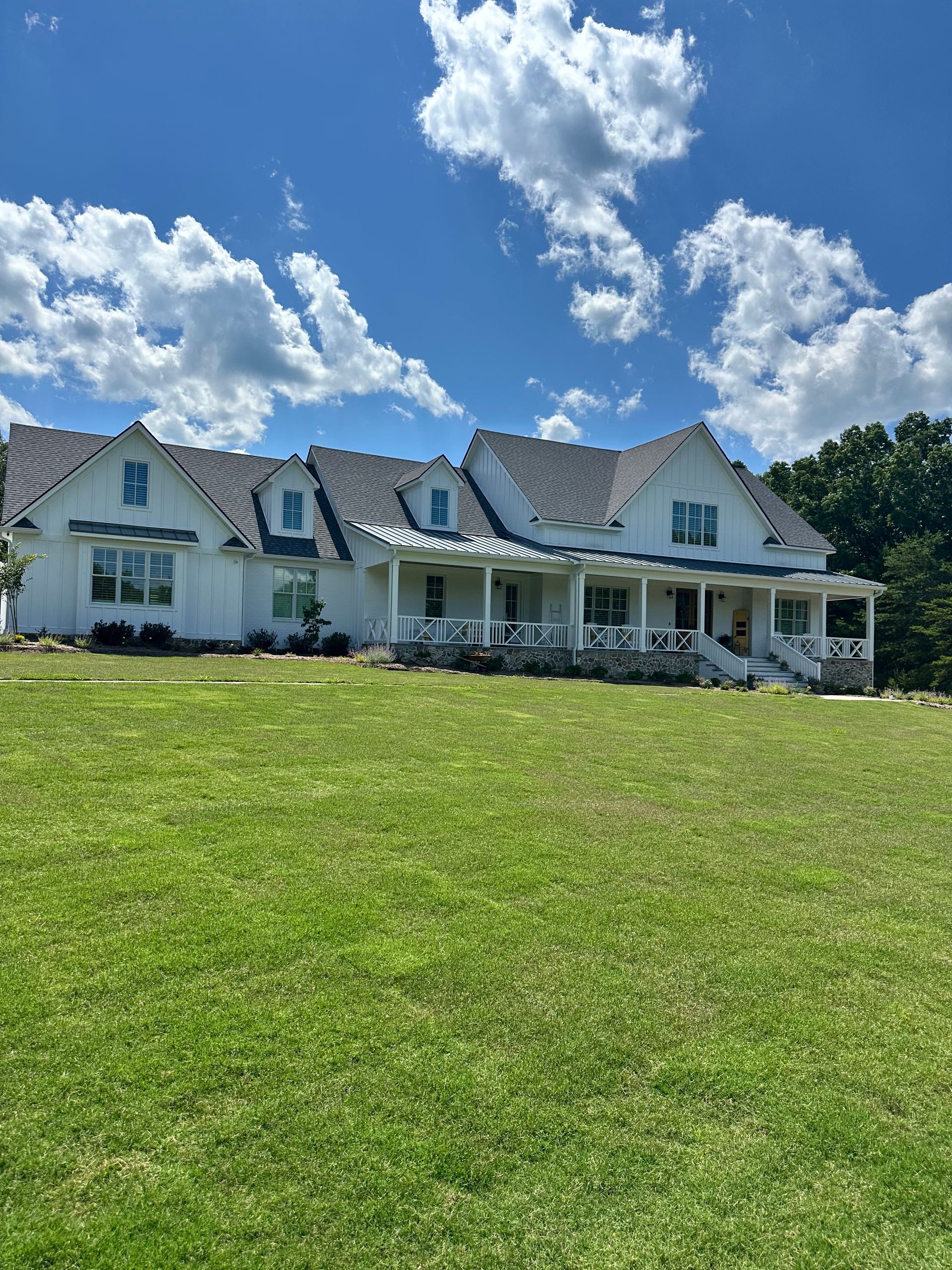 a large white house with a large porch is sitting on top of a lush green field .