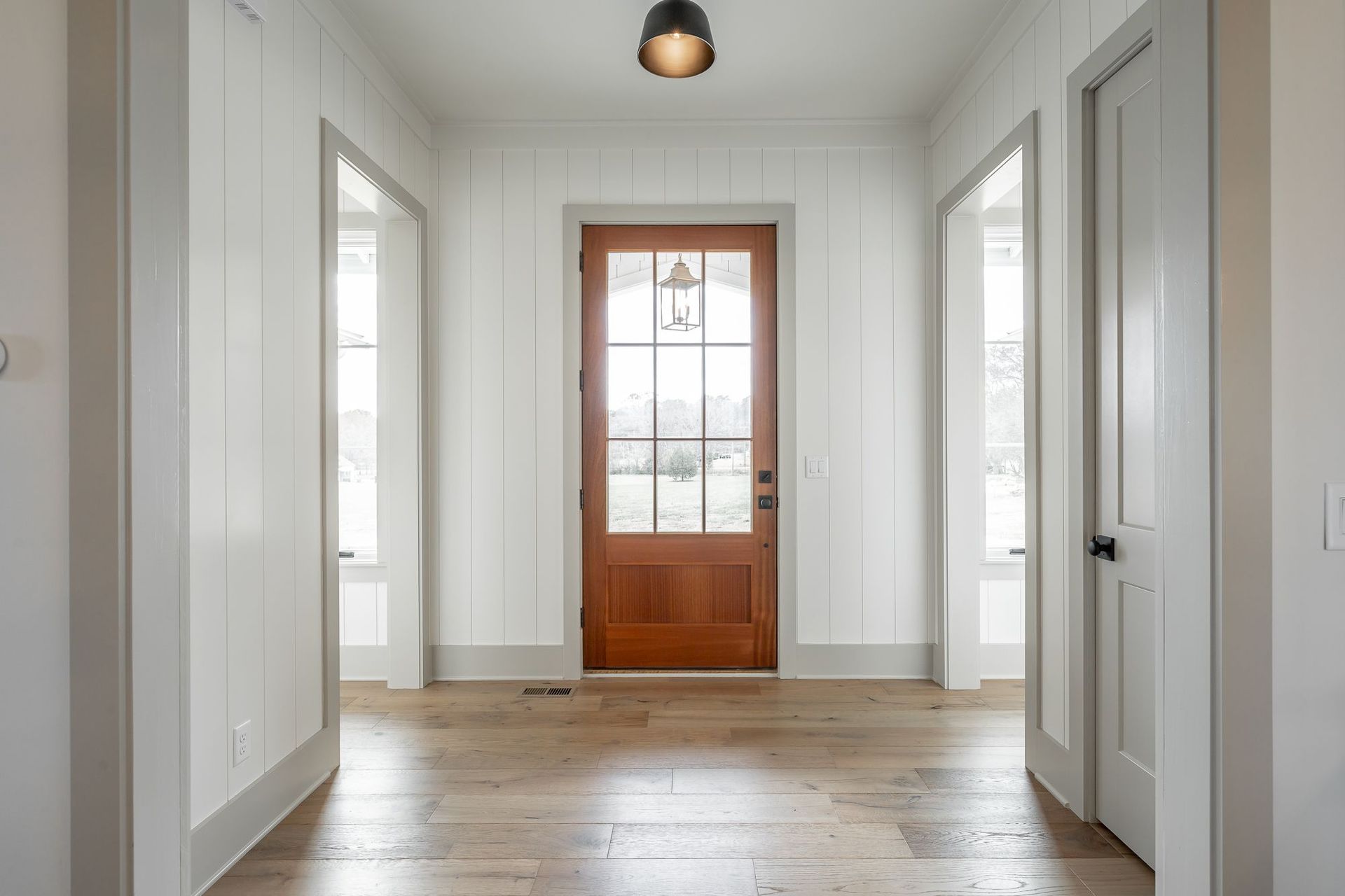 A hallway with a wooden door and hardwood floors in a house.