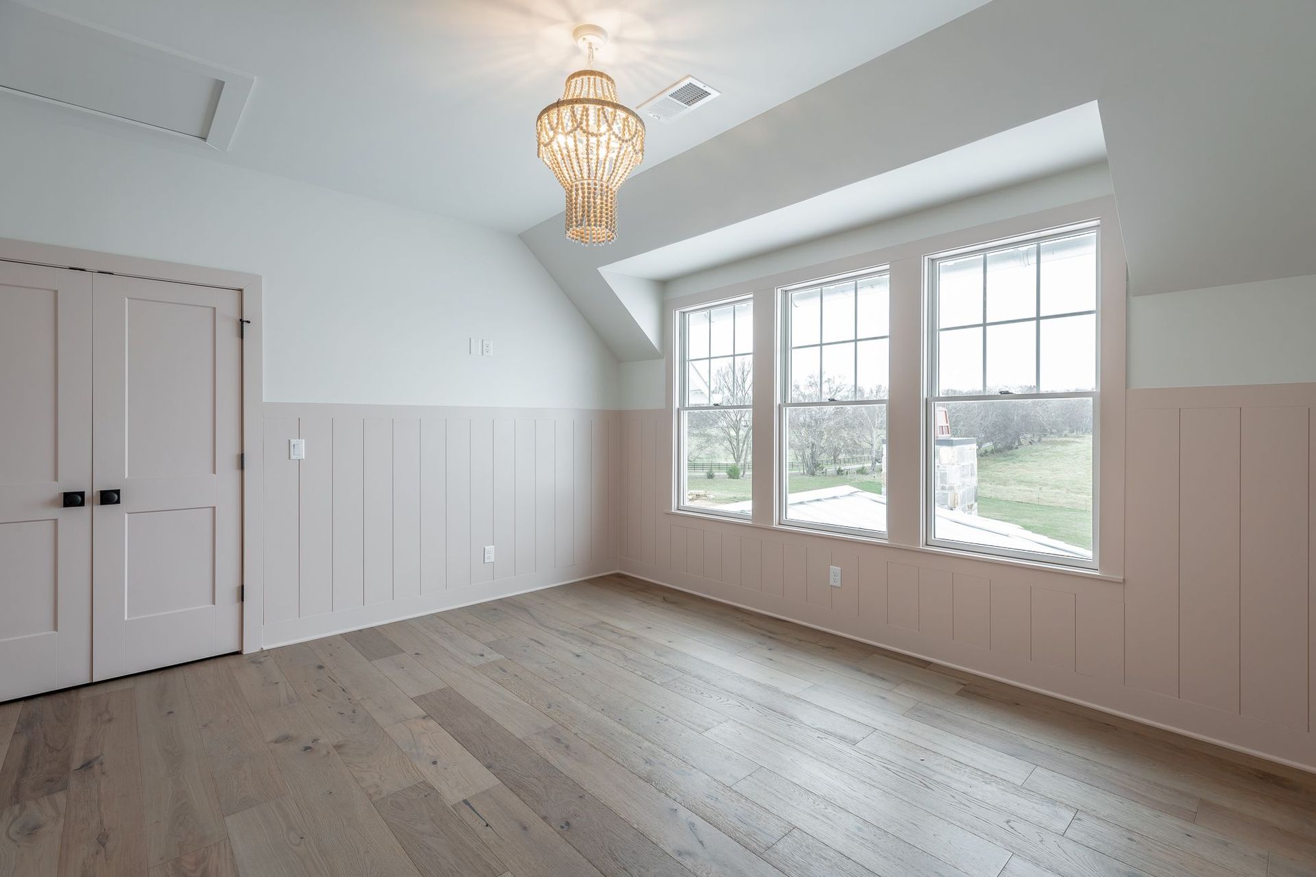 An empty room with pink walls and hardwood floors and a chandelier hanging from the ceiling.