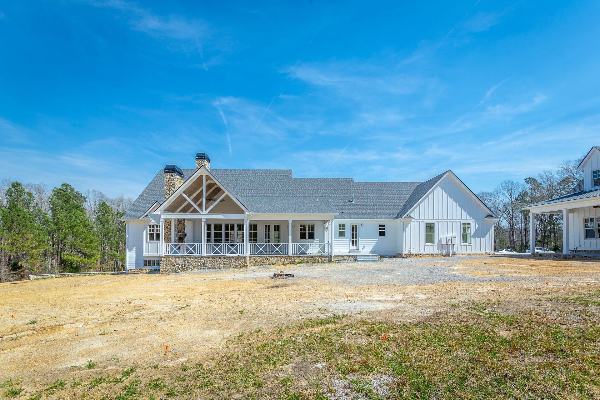 A large white house with a gray roof is sitting in the middle of a grassy field.