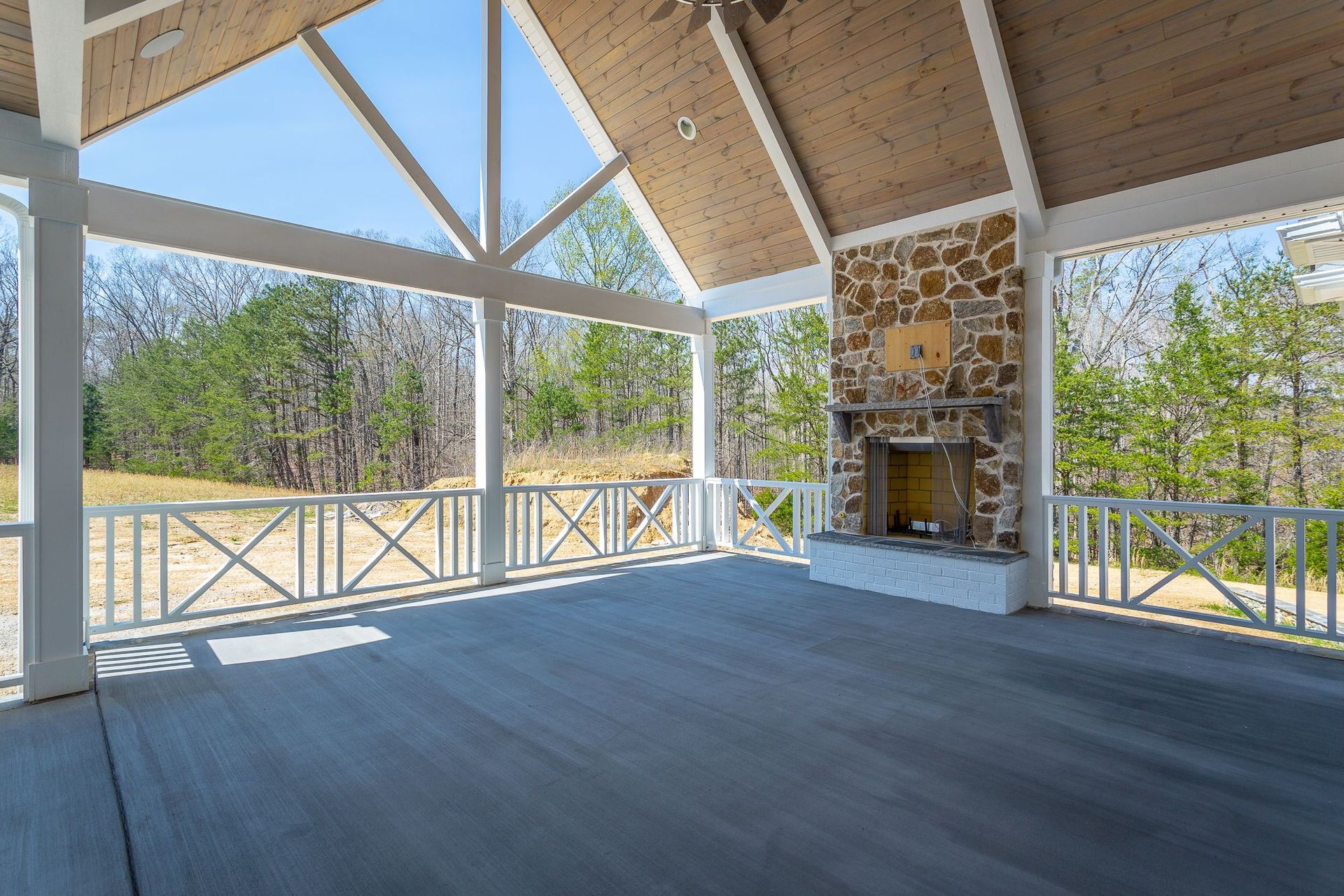 An empty porch with a stone fireplace and a wooden ceiling.