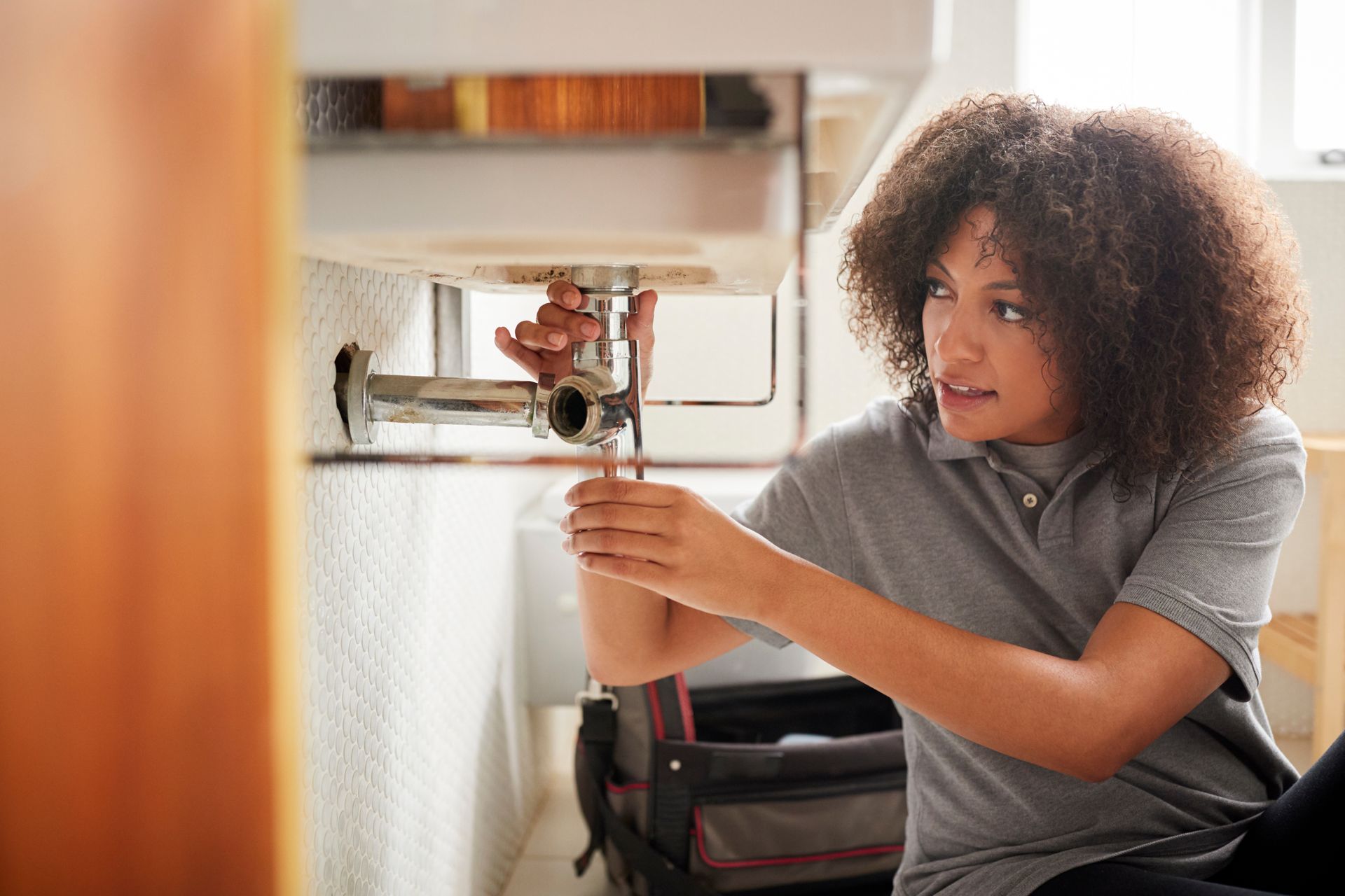 A young female plumber sitting on the floor expertly repairing a bathroom sink.