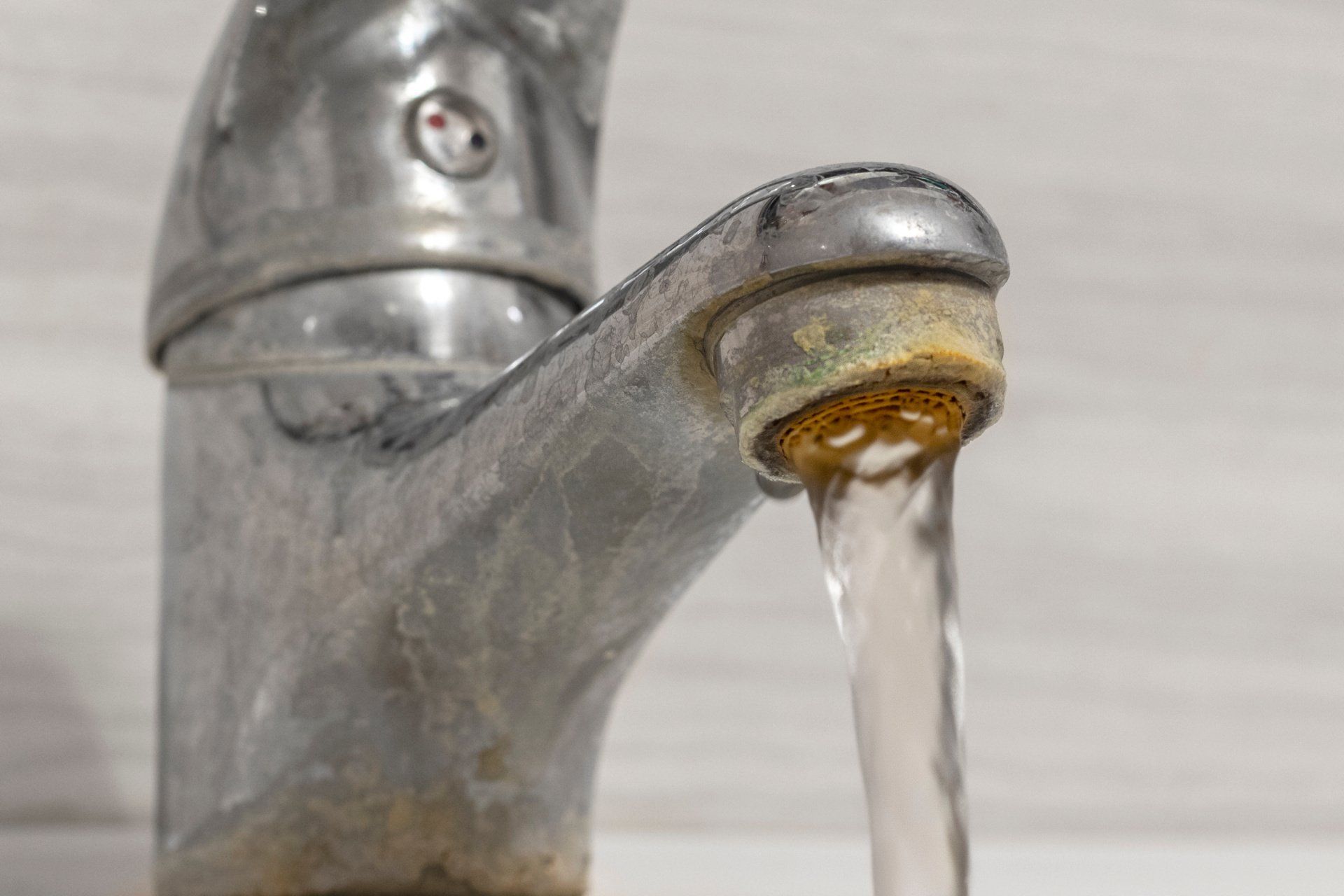 Calcium and grime buildup on an old bathroom sink faucet with hard water flow from the tap aerator.