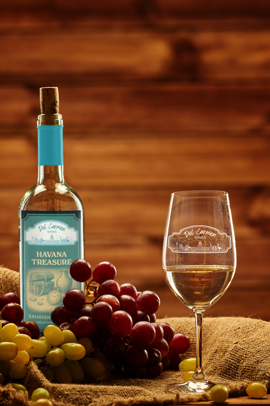 A bottle of white wine with a blue label, a glass of wine, and clusters of red and green grapes on a burlap surface.