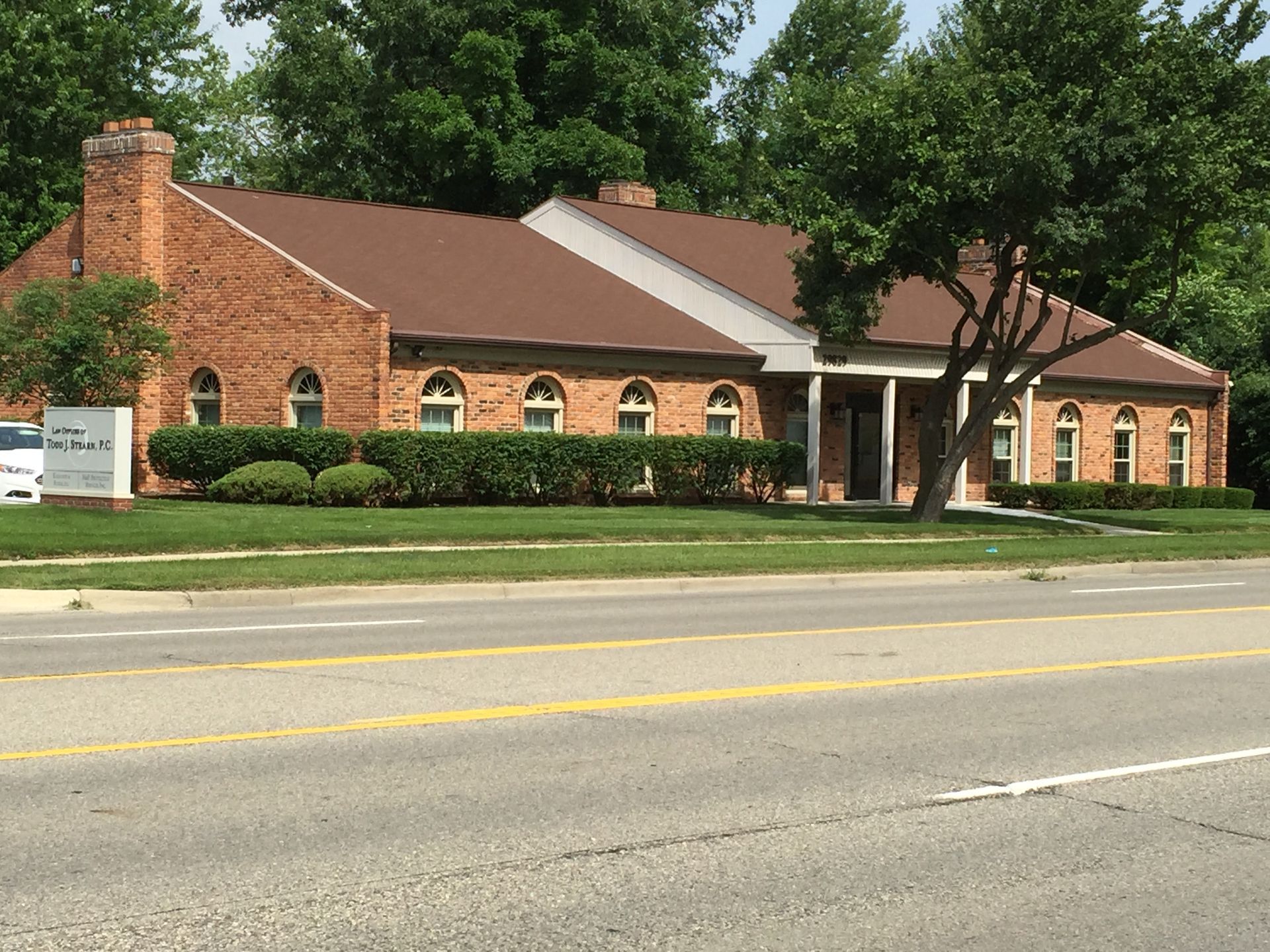 A brick building with a brown roof sits on the side of a road