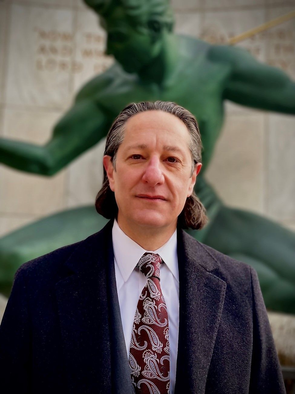 A man in a suit and tie stands in front of a statue