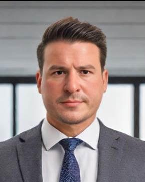 A man in a suit and tie is standing in front of a window.