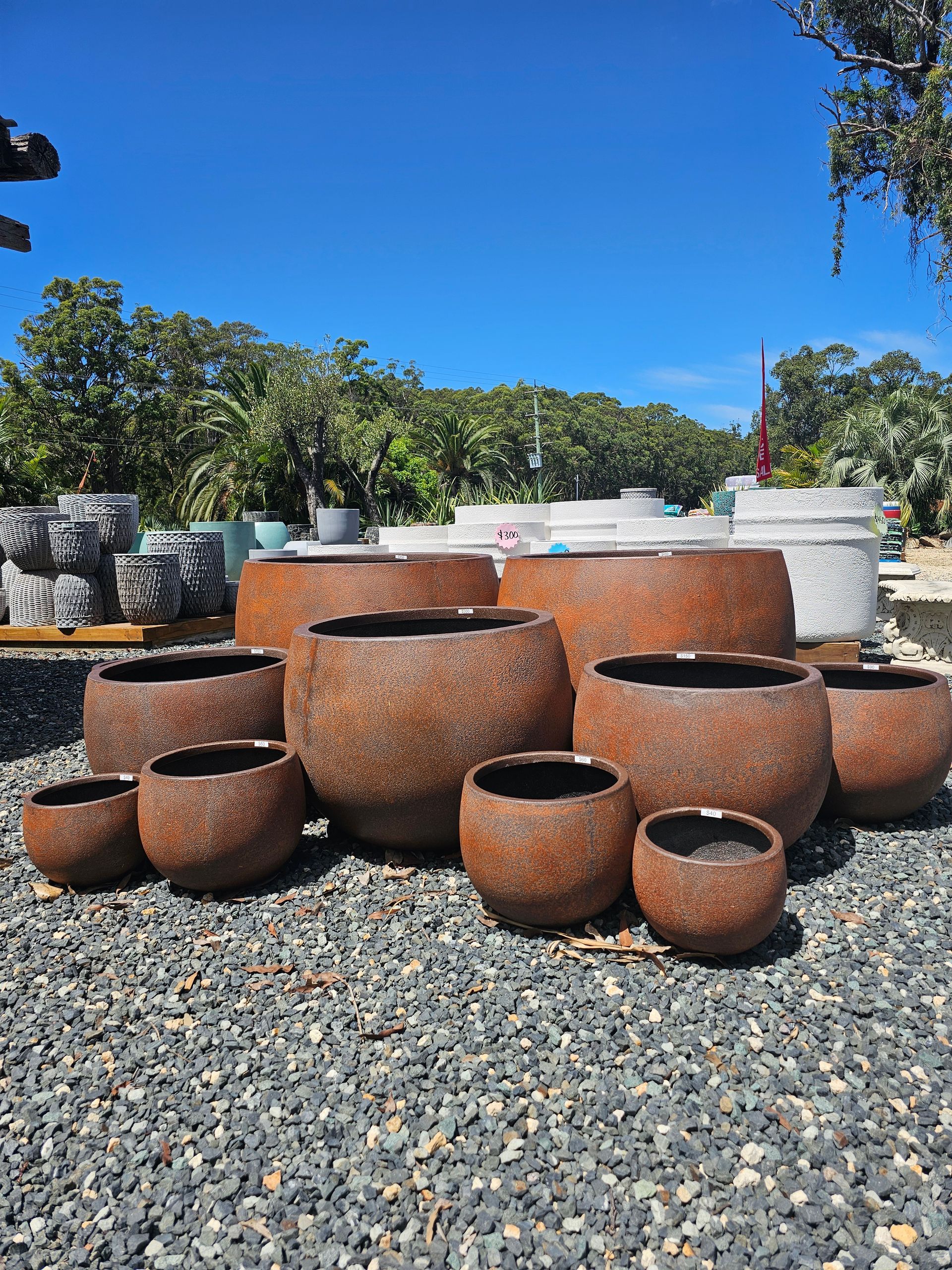 A collection of rusty, round planters on a gravel surface under a bright blue sky - Palms Landscape Supplies in Forster, NSW