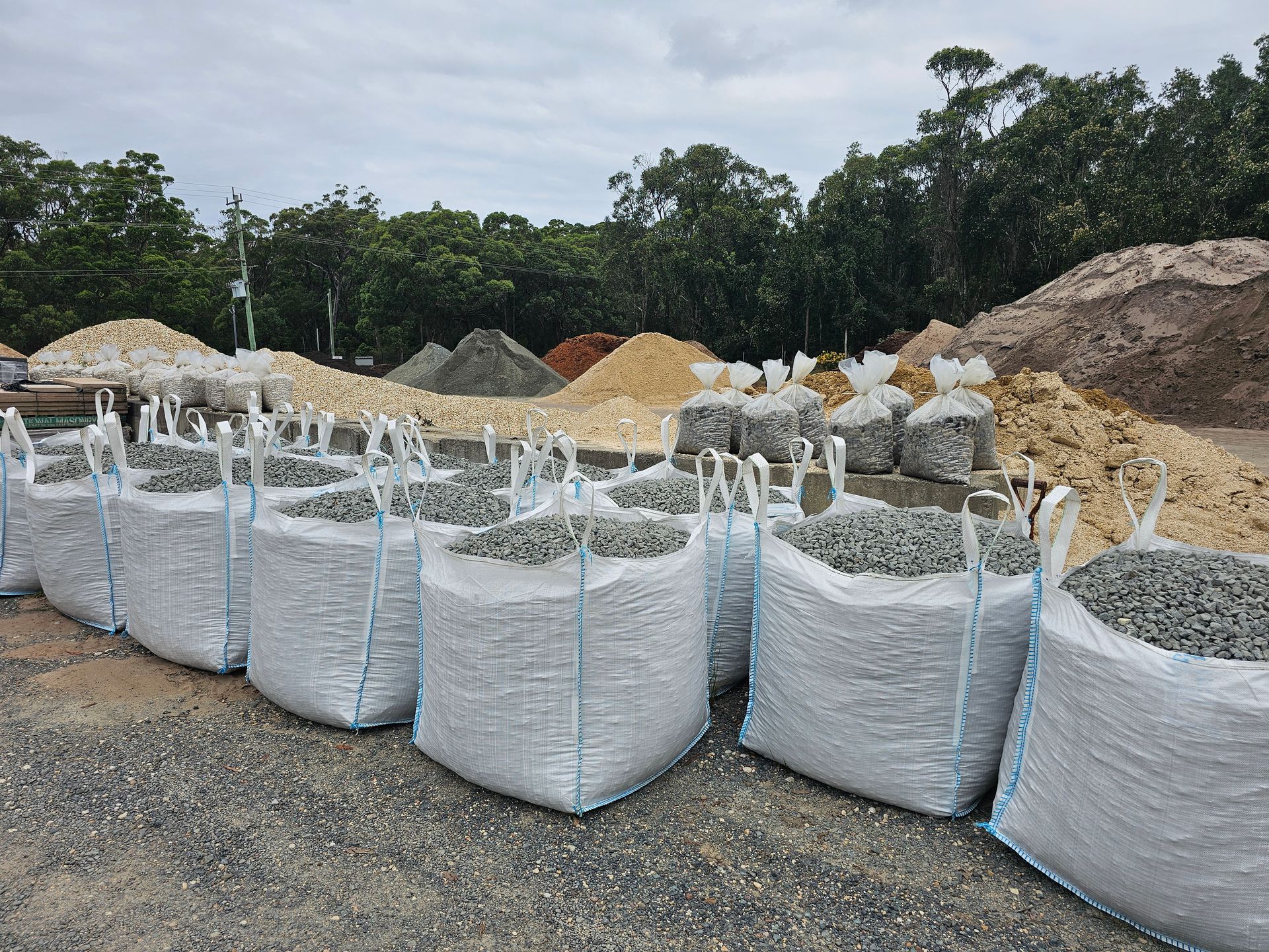 Large bags of gravel in a yard, with piles of other materials - Palms Landscape Supplies in Forster, NSW