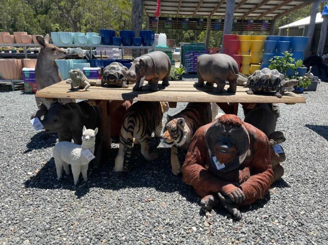 Statues of animals (hippo, tiger, orangutan) under a wooden table, outdoor setting - Palms Landscape Supplies in Forster, NSW