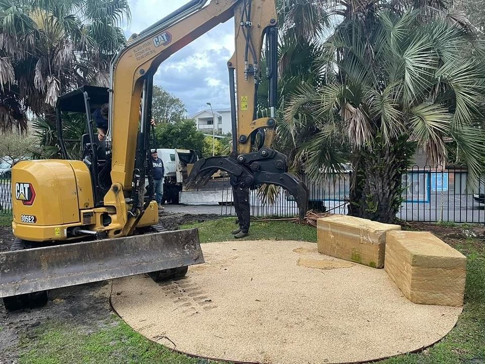 Yellow excavator placing straw bales in a circular sand area - Palms Landscape Supplies in Forster, NSW