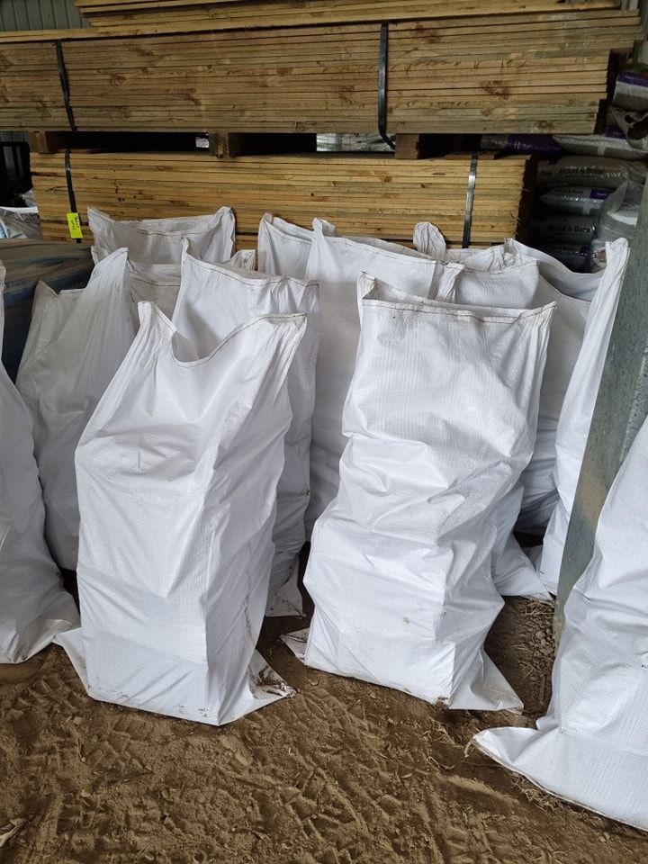 White bags of unknown contents piled in front of stacks of lumber in a warehouse setting - Palms Landscape Supplies in Forster, NSW