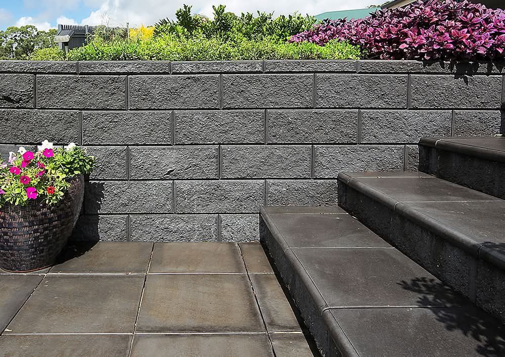 Grey brick retaining wall with steps and flower pots in a sunny outdoor setting - Palms Landscape Supplies in Forster, NSW