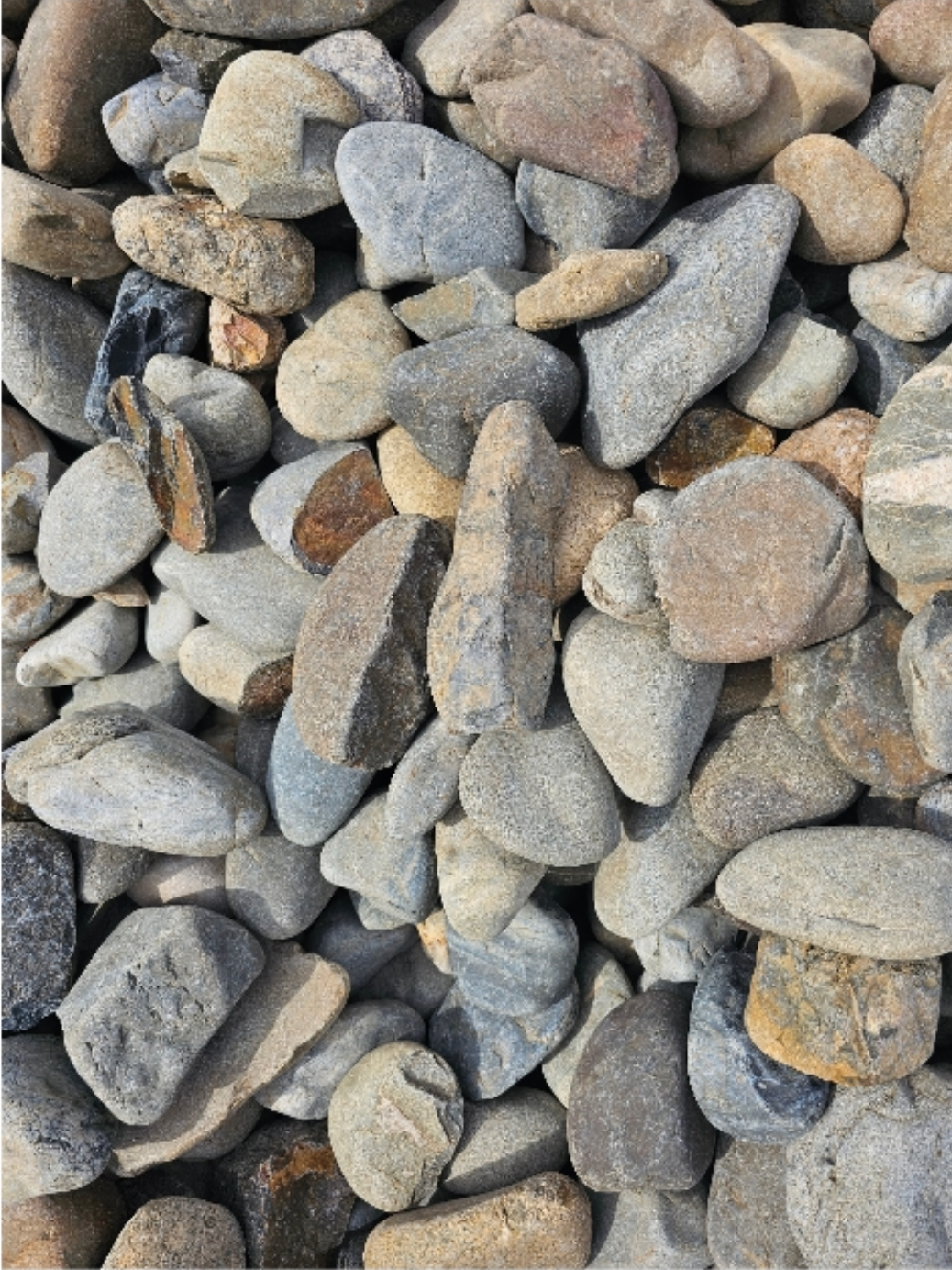 Pile of various-sized, smooth, rounded river rocks in shades of grey, brown, and tan - Palms Landscape Supplies in Forster, NSW