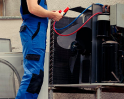 Un técnico de HVAC con un mono azul repara una unidad exterior, utilizando medidores.