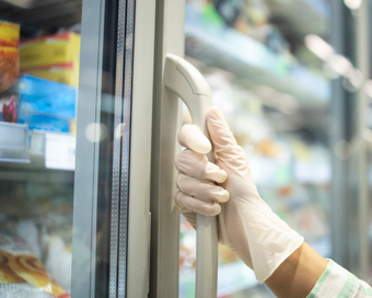 Mano en guante blanco abriendo la puerta de un congelador en una tienda.