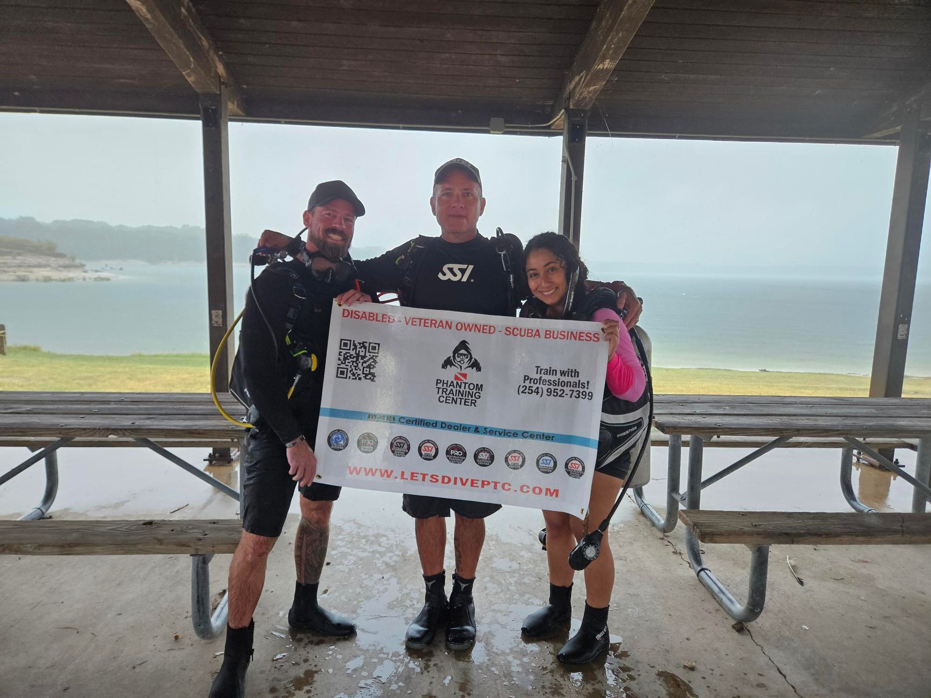 Scuba diver on boat, facing ocean, ready to dive. Clear turquoise water, blue sky, island in background.