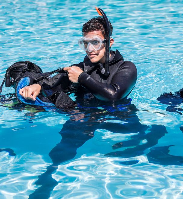 Man in scuba gear, snorkel, and mask in pool, adjusting equipment.