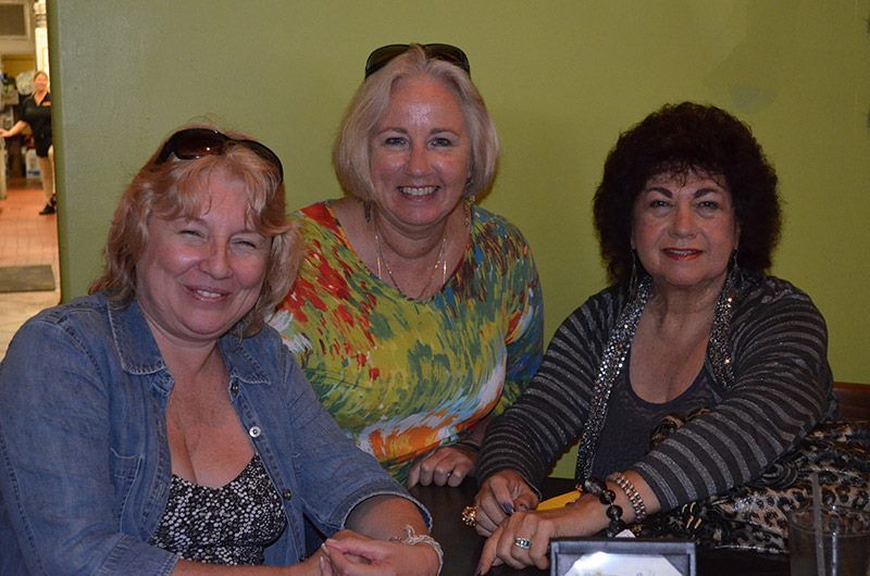 Three women are posing for a picture while sitting at a table.