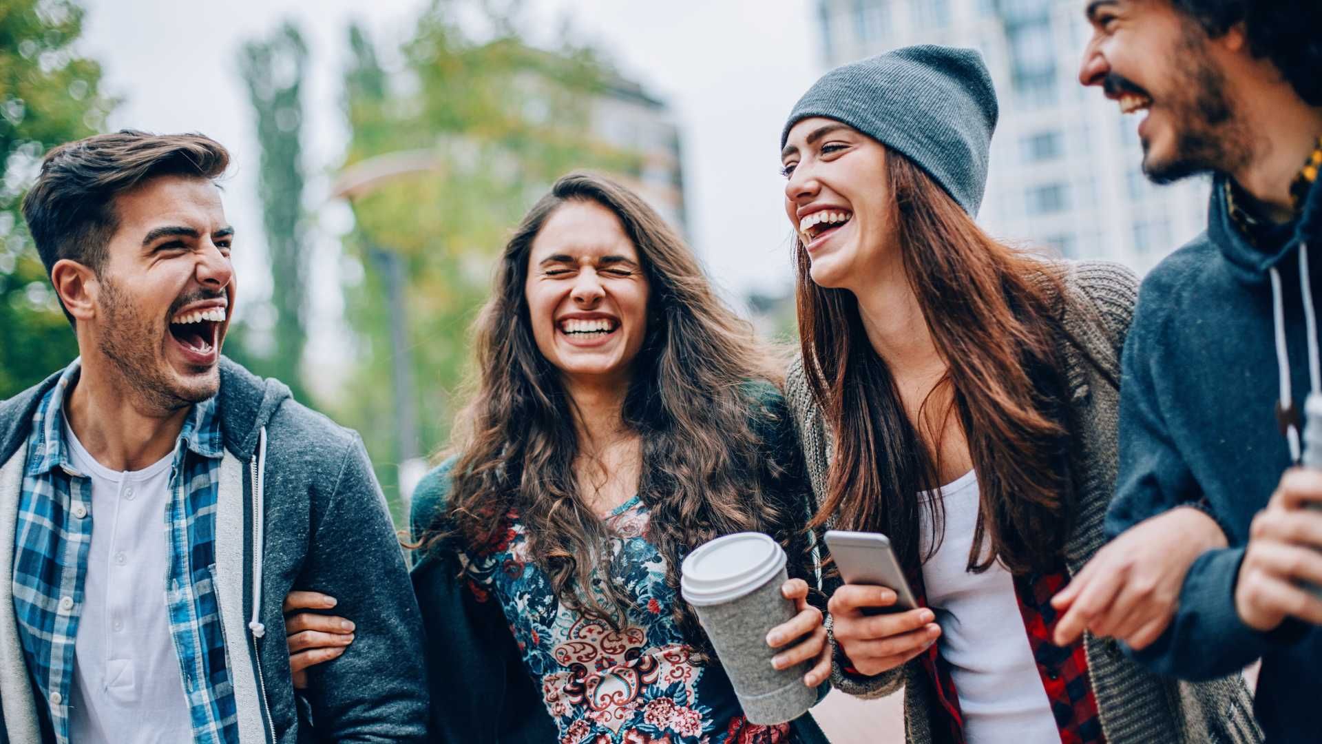A group of young people are laughing together while walking down the street.