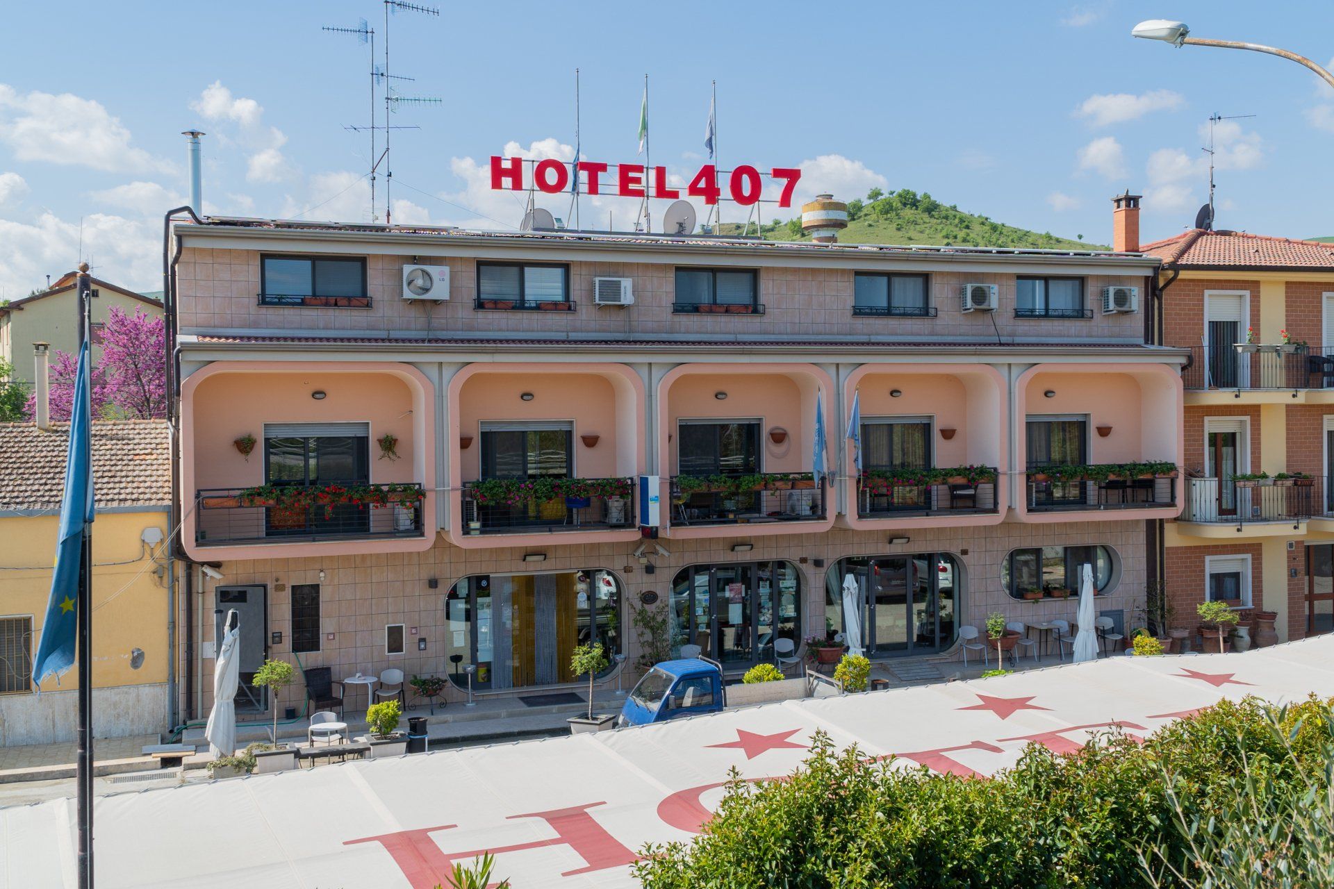 Hotel 407: edificio di tre piani con balconi, un'insegna rossa e vista sulla collina.