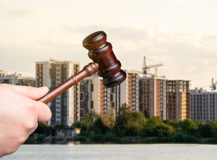 A hand holds a wooden gavel in front of blurry high-rise buildings, representing probate law. A hand holds a wooden gavel in front of blurry high-rise buildings, representing probate law.