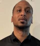 A man with a beard is wearing a black shirt and looking at the camera.