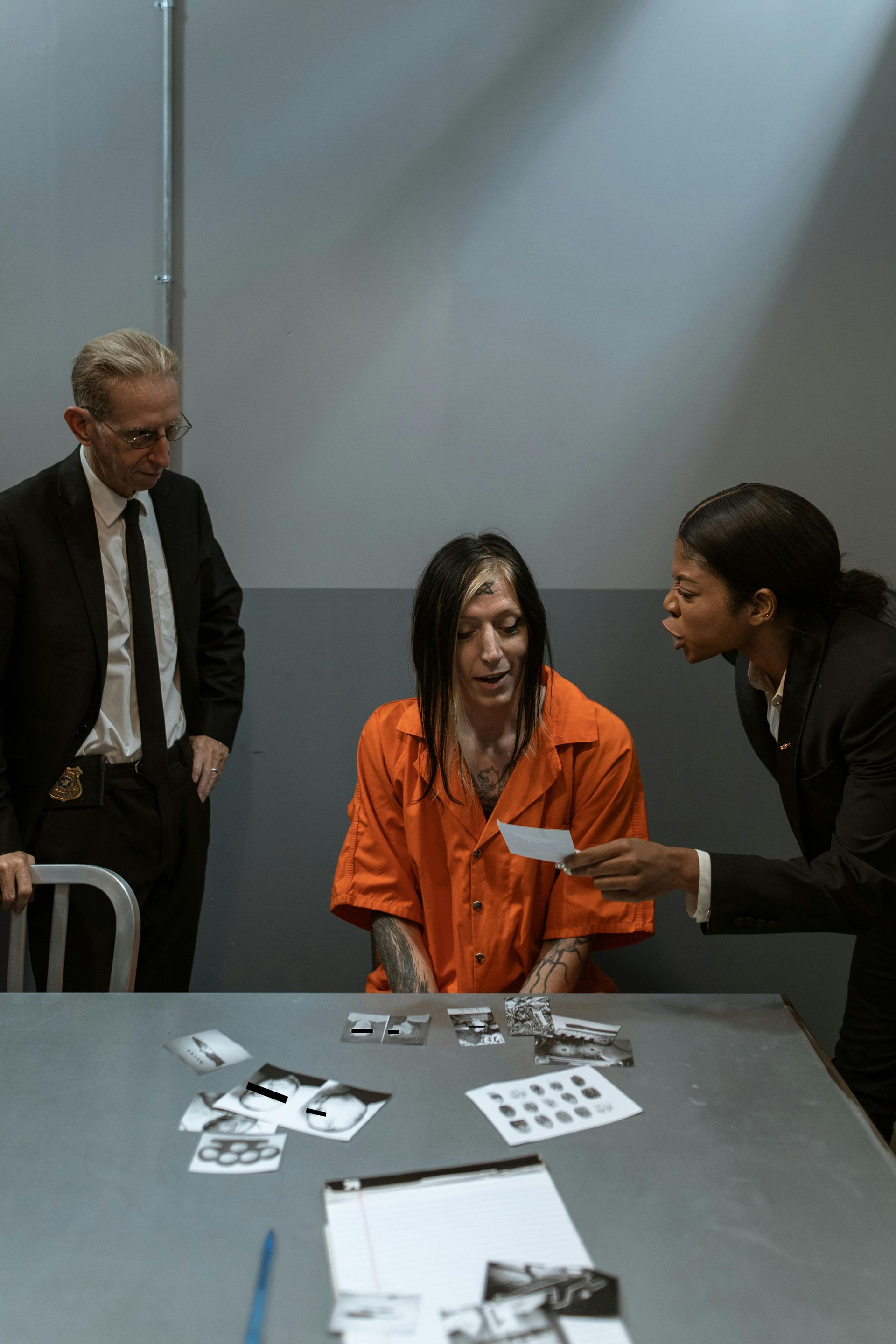 A man in an orange shirt is sitting at a table with two men in suits.