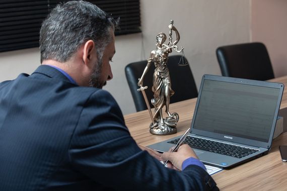 A man is sitting at a table with a laptop and a statue of justice.