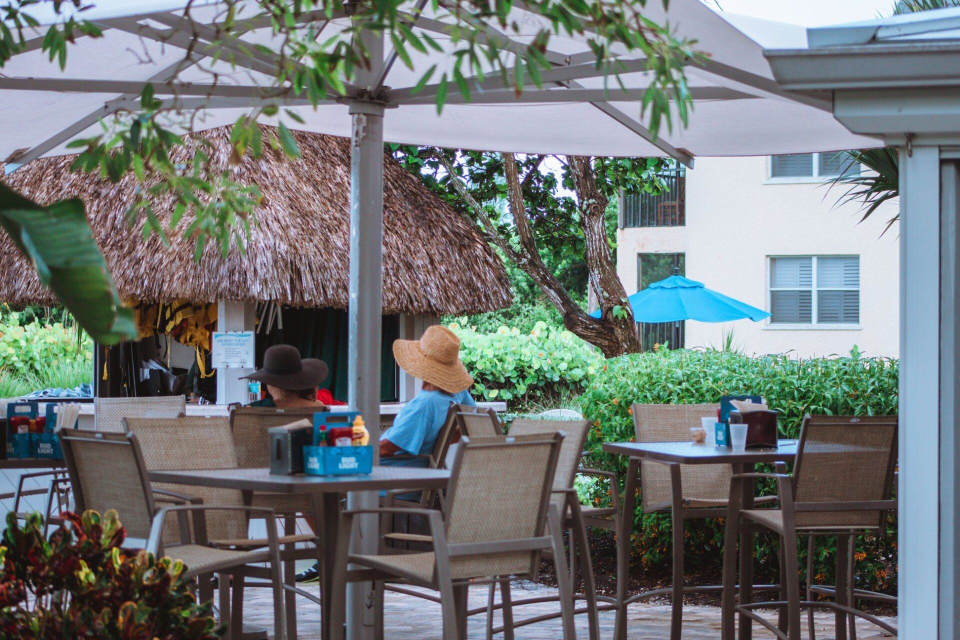 A woman in a hat is sitting at a table under an umbrella.