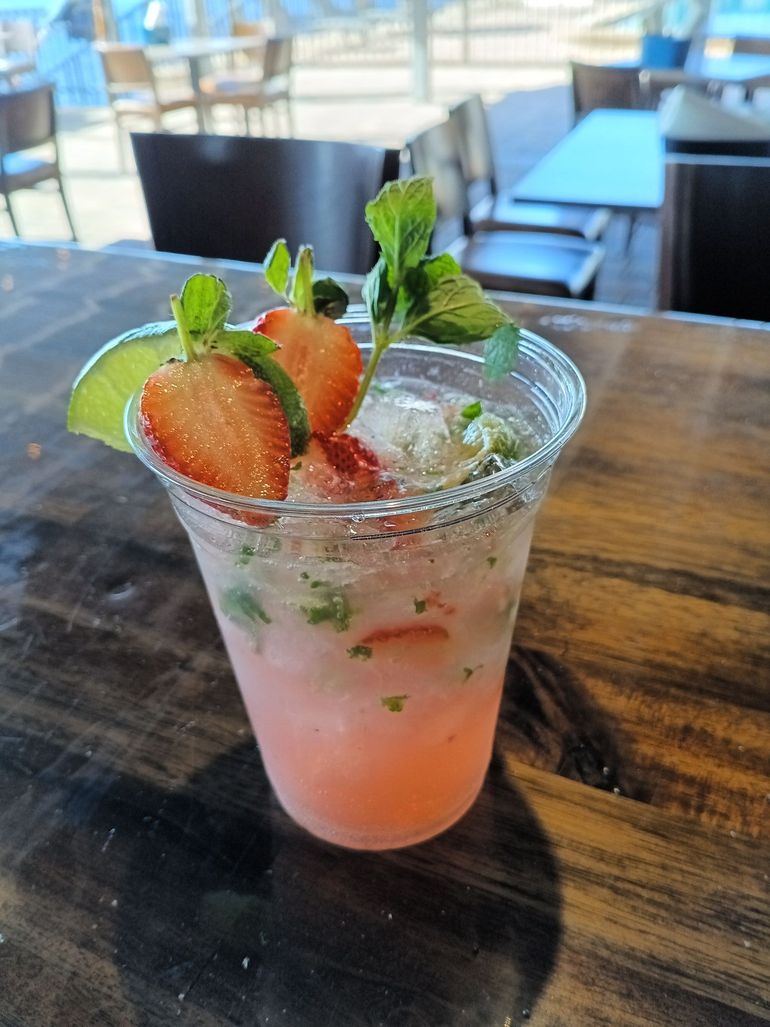 A pink drink with strawberries and limes in a plastic cup on a wooden table.