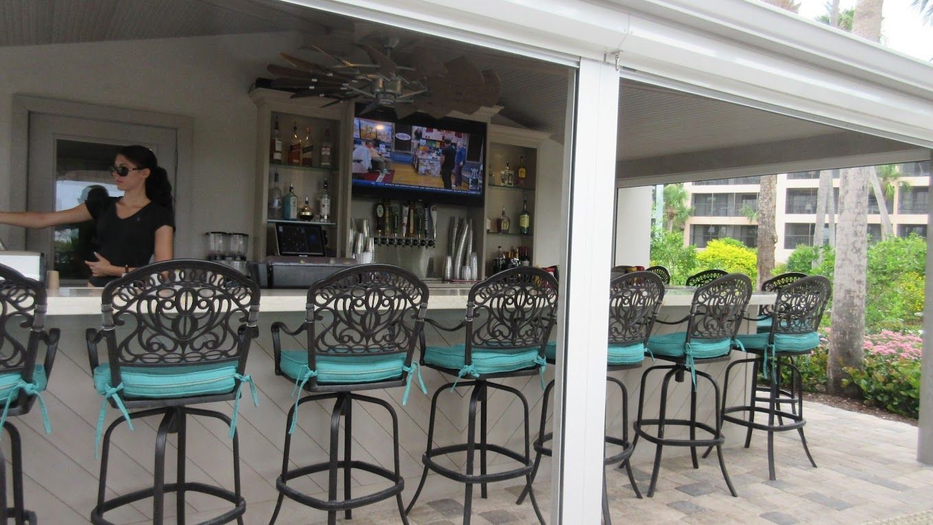 A woman is standing behind a bar with stools and a television.