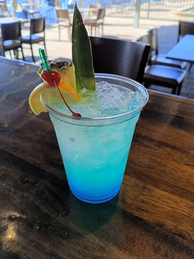 A blue drink in a plastic cup on a wooden table.