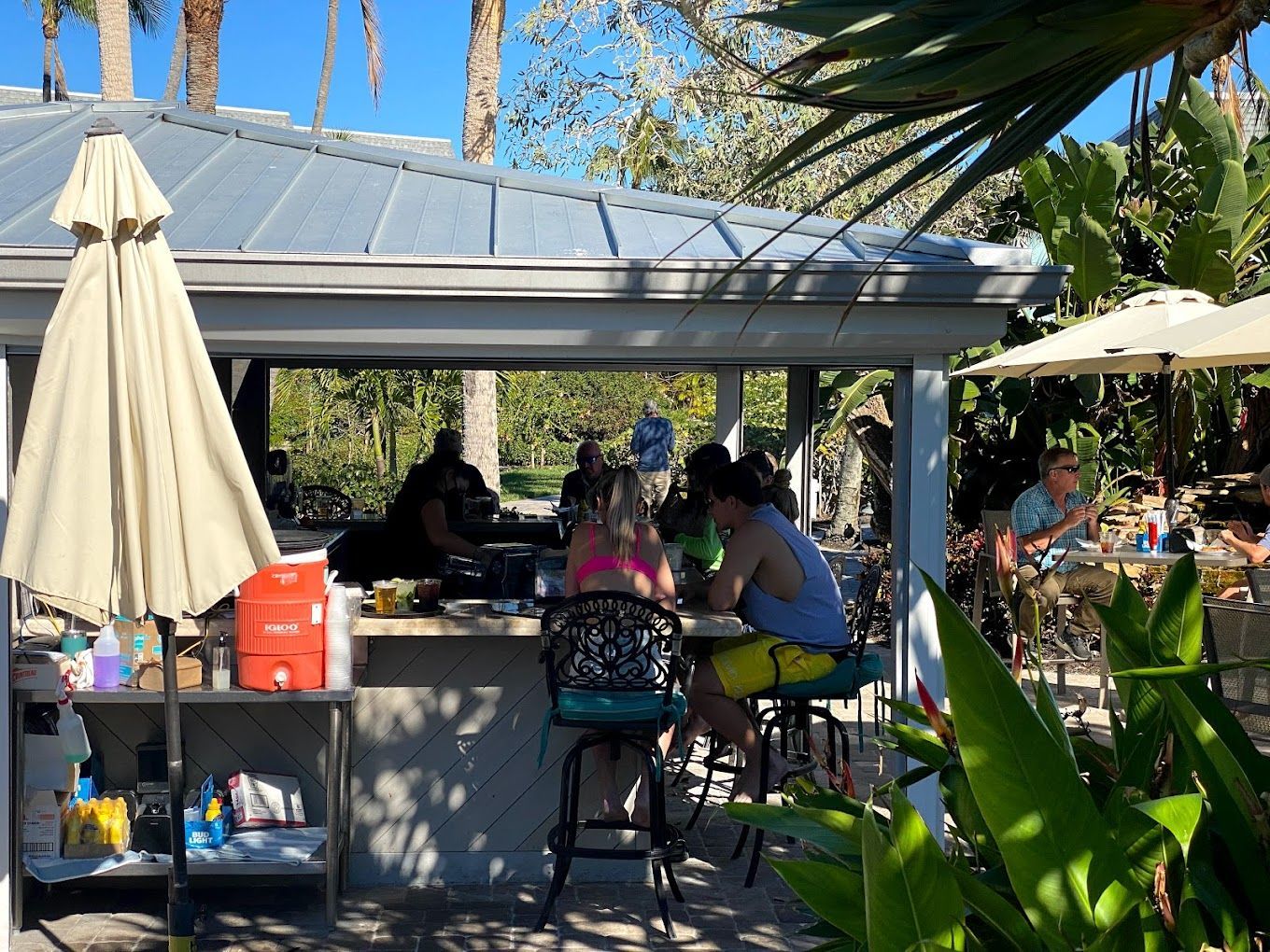 A group of people are sitting at tables under an umbrella at a restaurant.